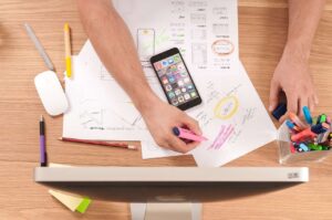 Alt Text: A user's hands are visible while working on SEO app development sketches with a smartphone on the desk 